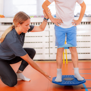 woman kneeling beside a person on a balance disc instructing them how to use it