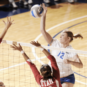 Girl spiking the volleyball over the net in a college volleyball net
